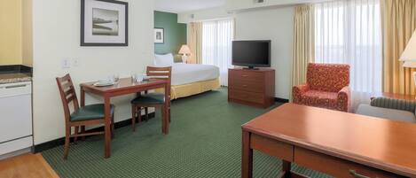 A hotel room with a bed, a TV, a dining table with chairs, a sofa, and a window with curtains.