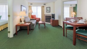 A hotel room with a green carpet, a sofa, a dining table with chairs, a TV, and a fireplace. - Residence Inn by Marriott Oklahoma City South (Oklahoma City)