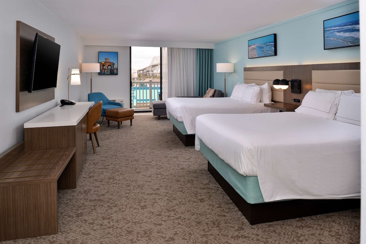 A hotel room with two beds, a desk, a chair, a TV, and a view of a pool and building.