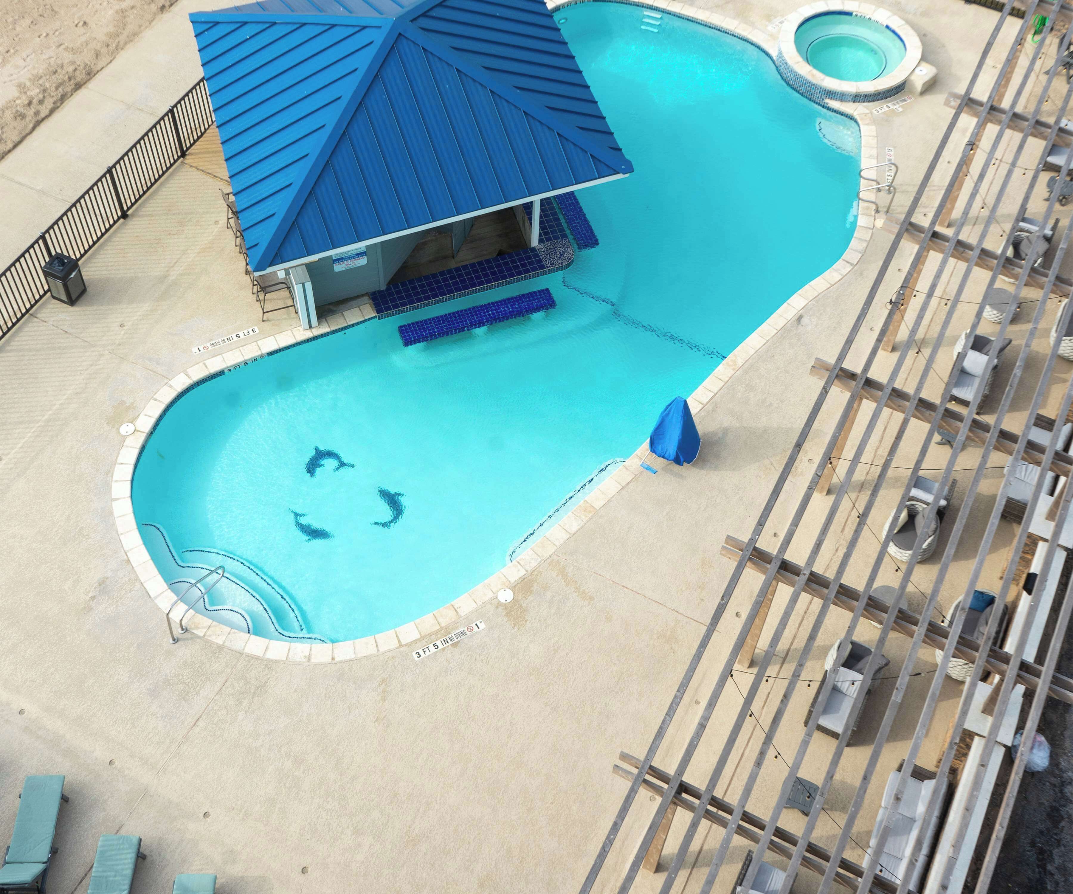 A swimming pool with a blue roof structure, a diving board, and a small circular hot tub.