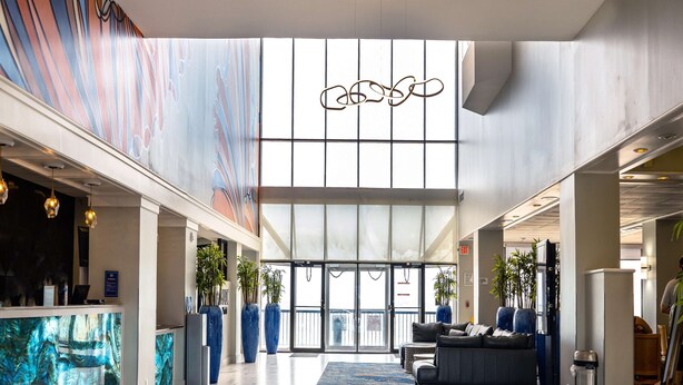 A spacious lobby with a marble floor, a reception desk, seating area, and large windows allowing natural light.