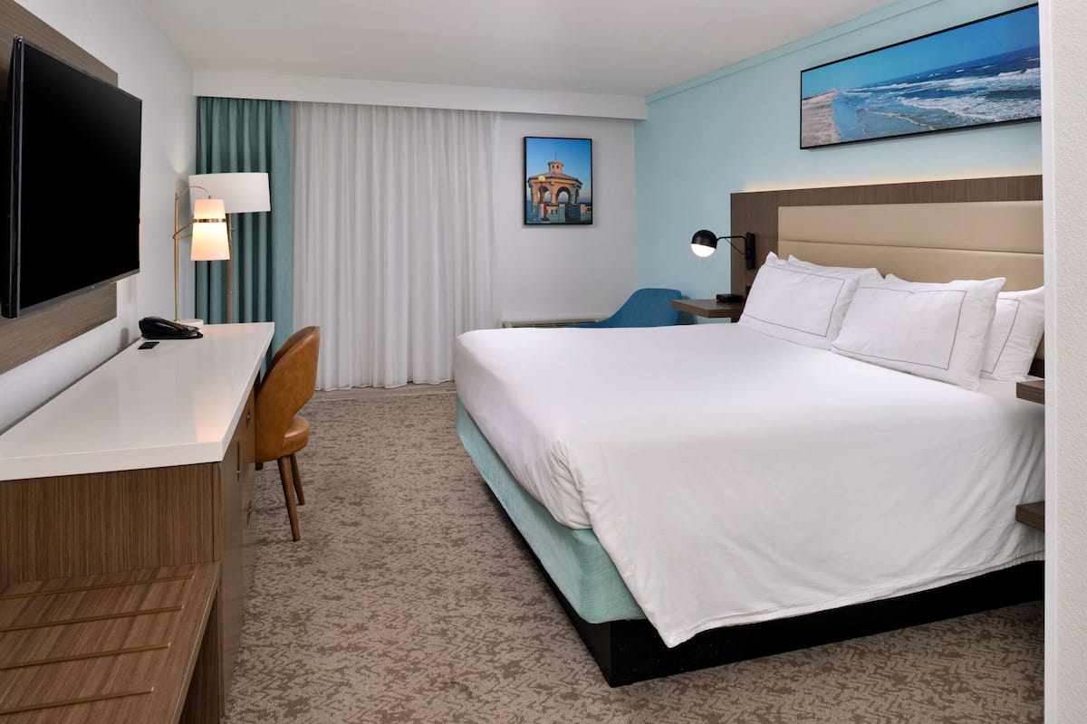 A hotel room with a bed, desk, chair, and a TV.