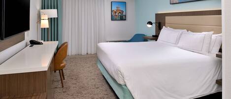 A hotel room with a bed, desk, chair, and a TV.