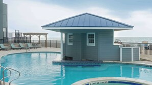 A pool area with lounge chairs, a hot tub, and a small building with a blue roof.
