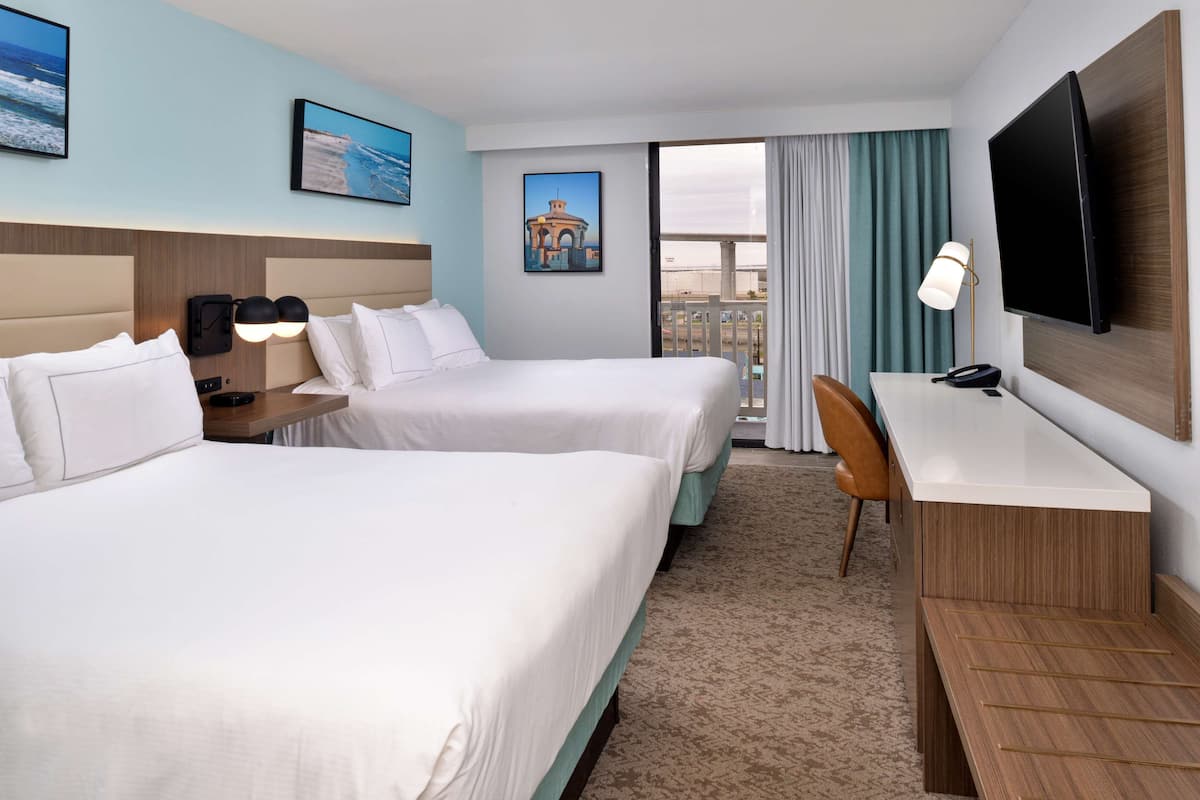 A hotel room with two beds, a desk, a TV, and a window with curtains.