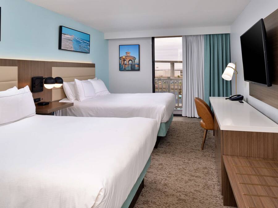 Een hotelkamer met twee bedden, een bureau, een televisie en een raam met gordijnen.