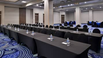 A conference room with long tables, chairs, water bottles, and a blue carpet.
