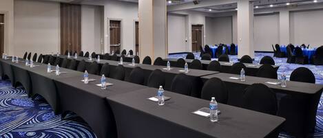 A conference room with long tables, chairs, water bottles, and a blue carpet.