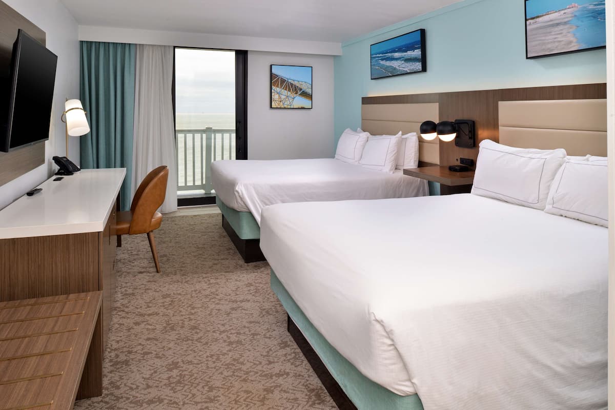 A hotel room with two beds, a desk, a chair, a TV, and a balcony with a view.