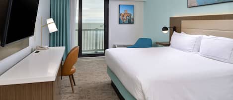 A hotel room with a bed, a desk, a chair, a TV, and a balcony with a view of the ocean.