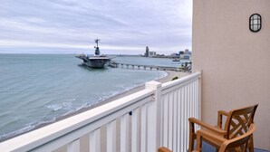 A balcony with a view of the ocean, a pier, and a city skyline in the distance.