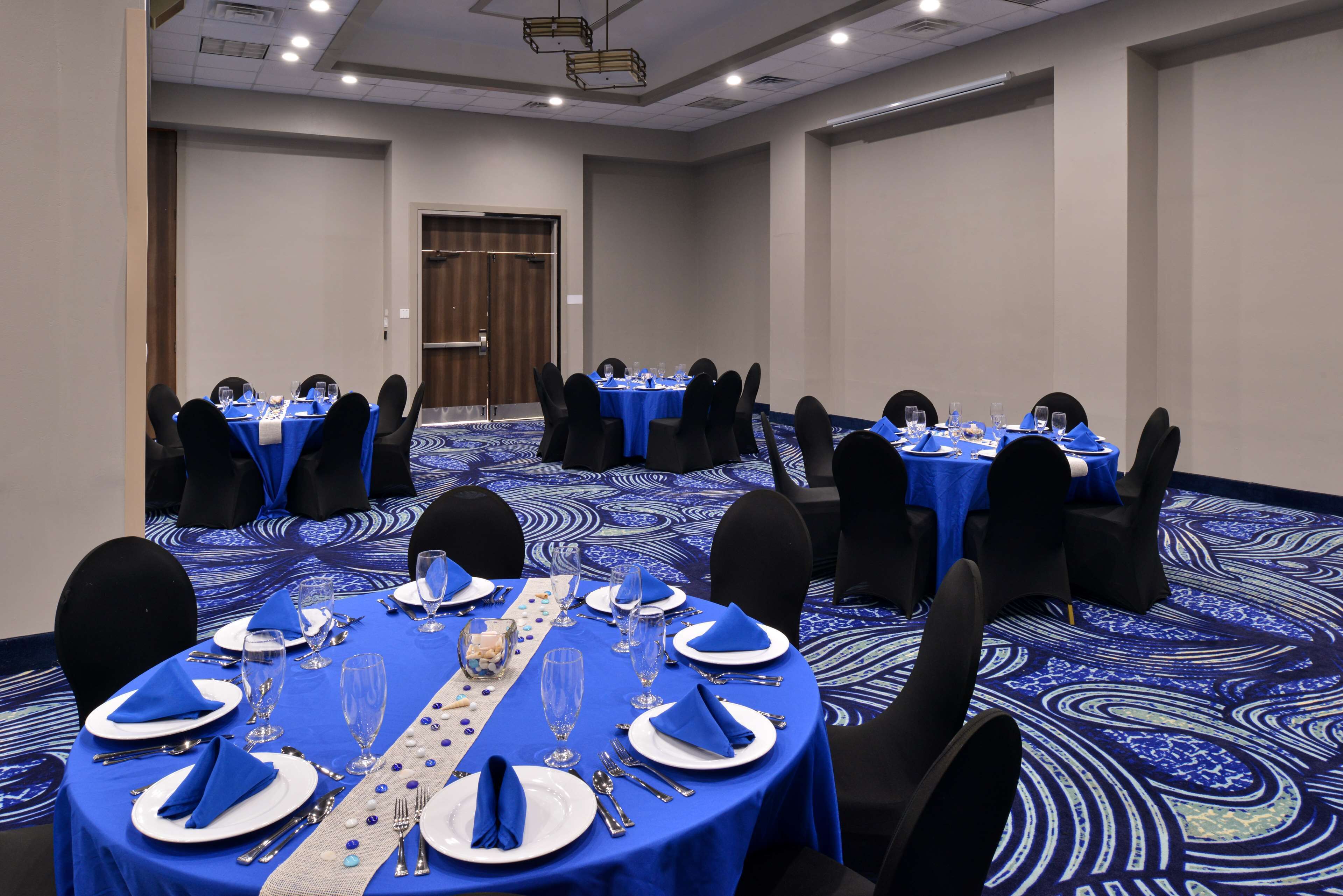A conference room with round tables, blue tablecloths, and black chairs.