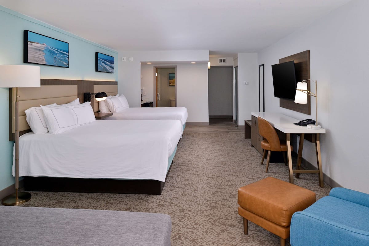 A hotel room with two beds, a desk, a chair, and a TV.