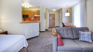 A hotel room with a kitchenette, a sofa with a red throw pillow, and a bed with a white comforter. - TownePlace Suites by Marriott Raleigh Cary-Weston Parkway (Cary)