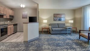 A modern hotel room with a kitchenette, a gray sofa, two lamps, and a patterned carpet. - TownePlace Suites by Marriott Raleigh Cary-Weston Parkway (Cary)