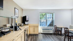 A kitchen with a stove, toaster, and microwave, a dining table with chairs, and a window with a view of trees. - TownePlace Suites by Marriott Raleigh Cary-Weston Parkway (Cary)