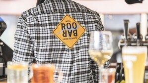 A person wearing a plaid shirt with a patch that says "Next... BAR HAUSER ST. MORITZ".