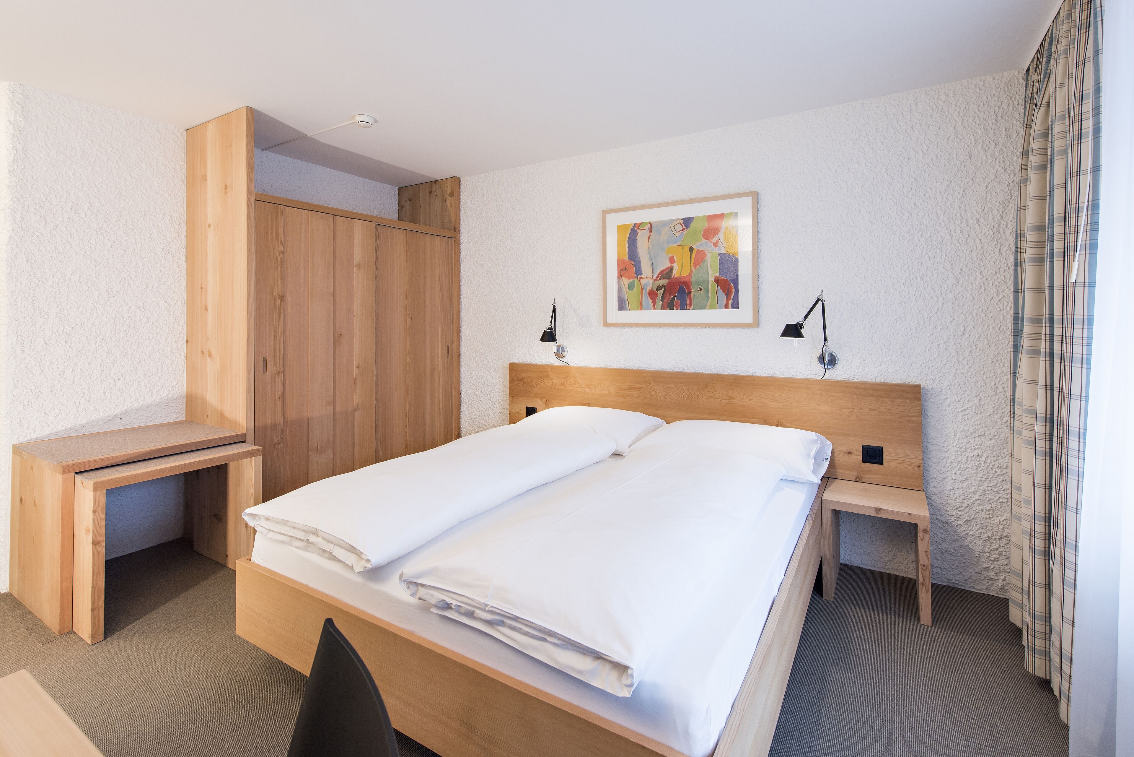 Un dormitorio ordenado con una cama de madera, un escritorio y una mesita de noche.