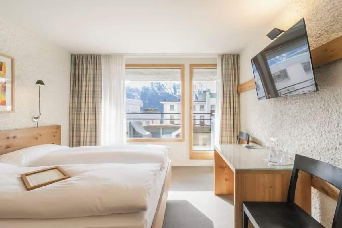 Habitación de hotel con cama, escritorio, televisor y vista a las montañas.