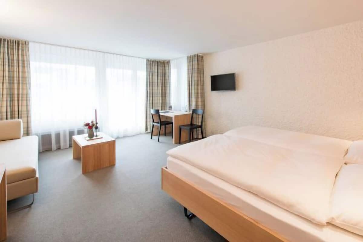 Habitación de hotel con cama, escritorio, silla y televisión en la pared.