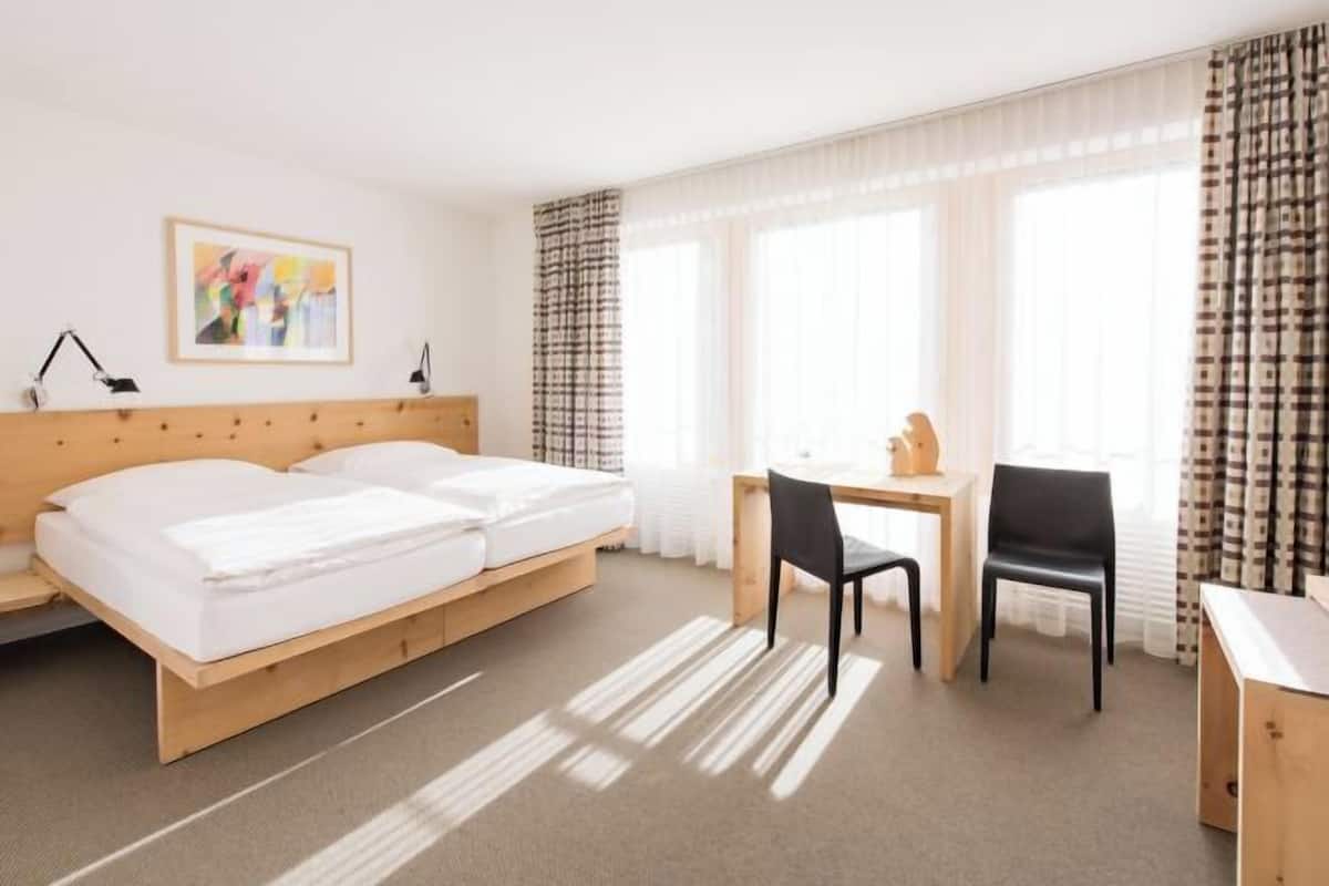 Una habitación de hotel con una cama doble, un escritorio con silla y una ventana con cortinas.