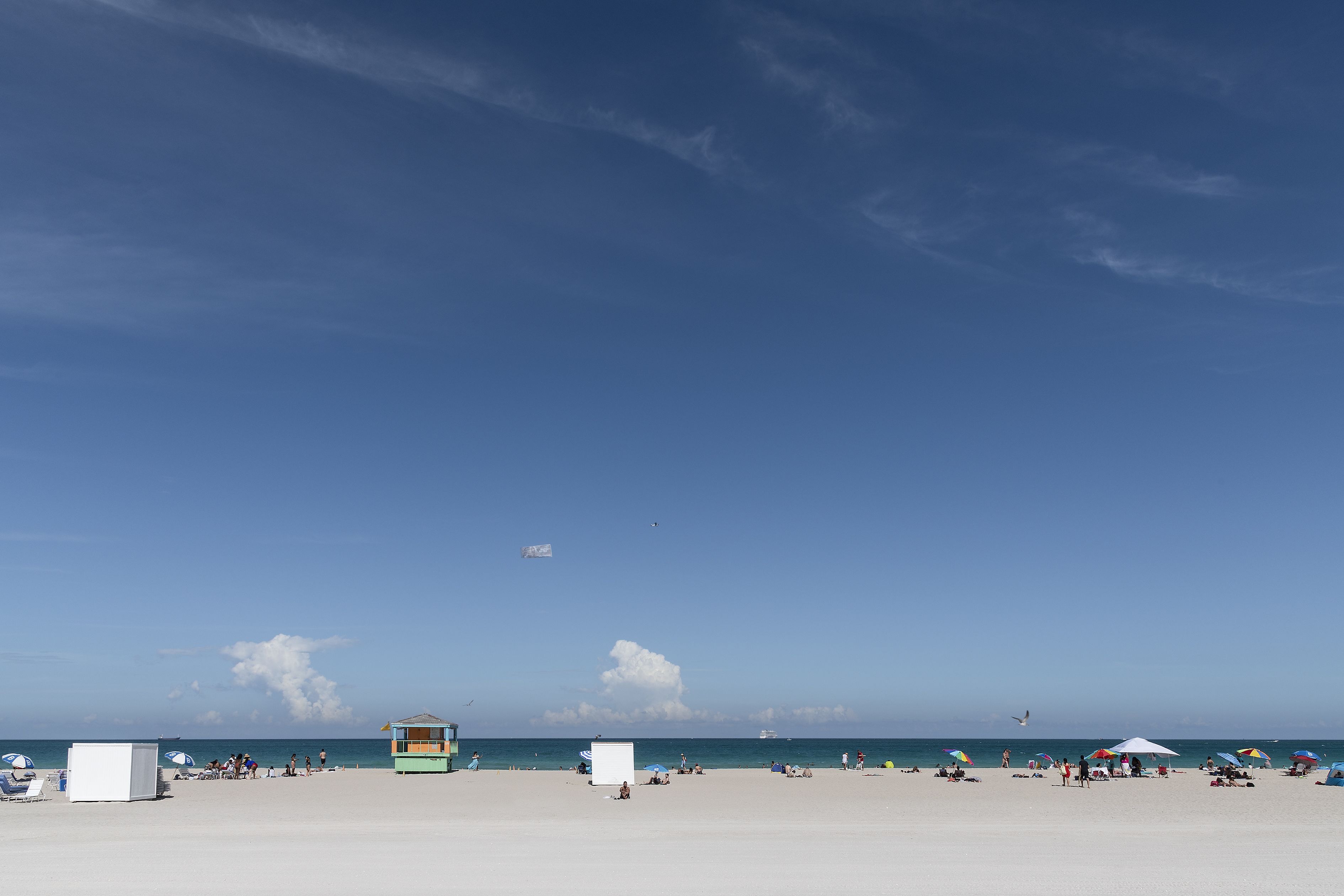 Ein Strand mit einem Rettungsturm, Sonnenschirmen und entspannenden Menschen.