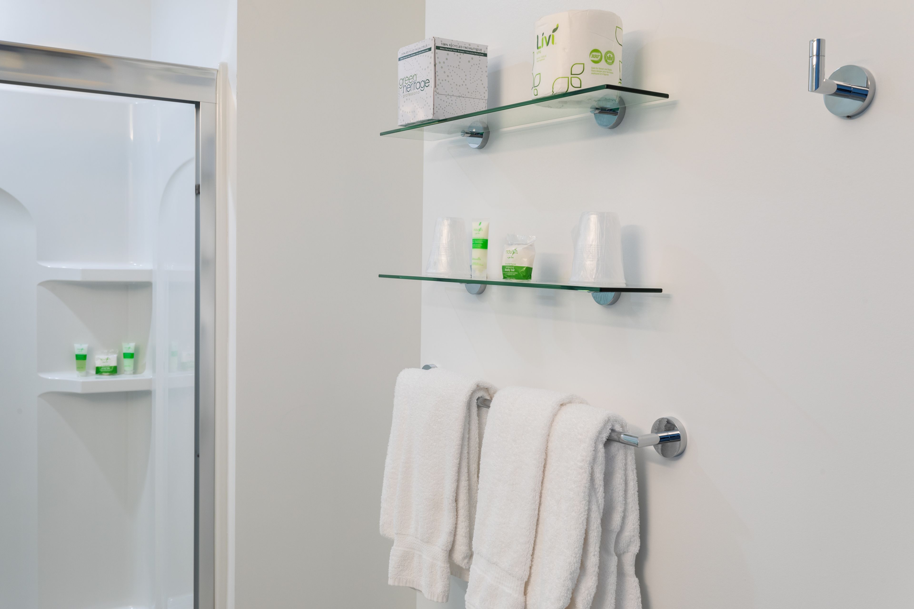 A bathroom with a glass shower enclosure, a white towel rack with towels, and shelves with toiletries.