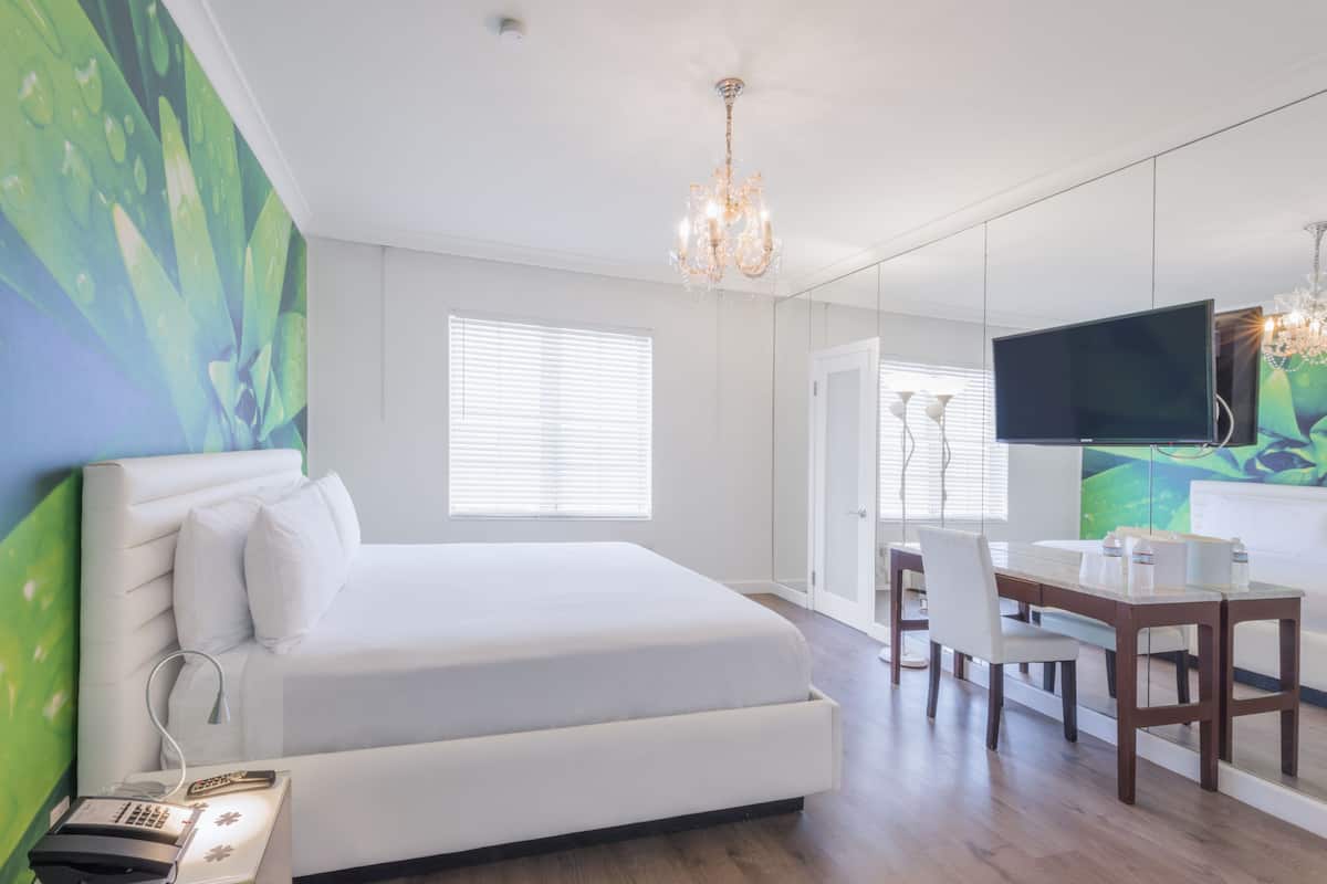 A hotel room with a large bed, a desk with a chair, a television, and a chandelier.