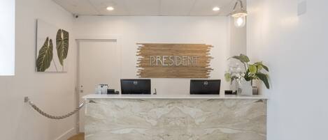 A reception desk with a marble top, two computers, a 'PRESIDENT' sign, a plant, and a hanging light fixture.