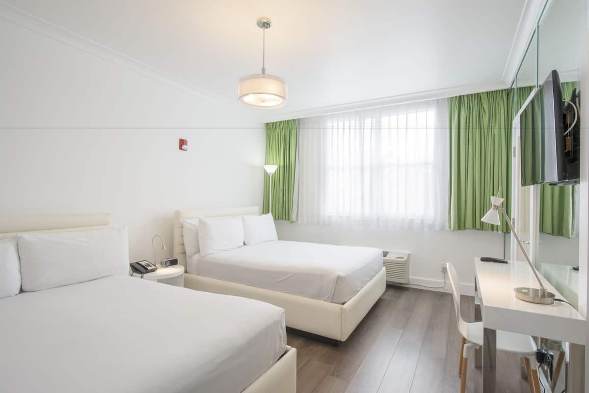A hotel room with two beds, a desk, a chair, a TV, and a window with green curtains.