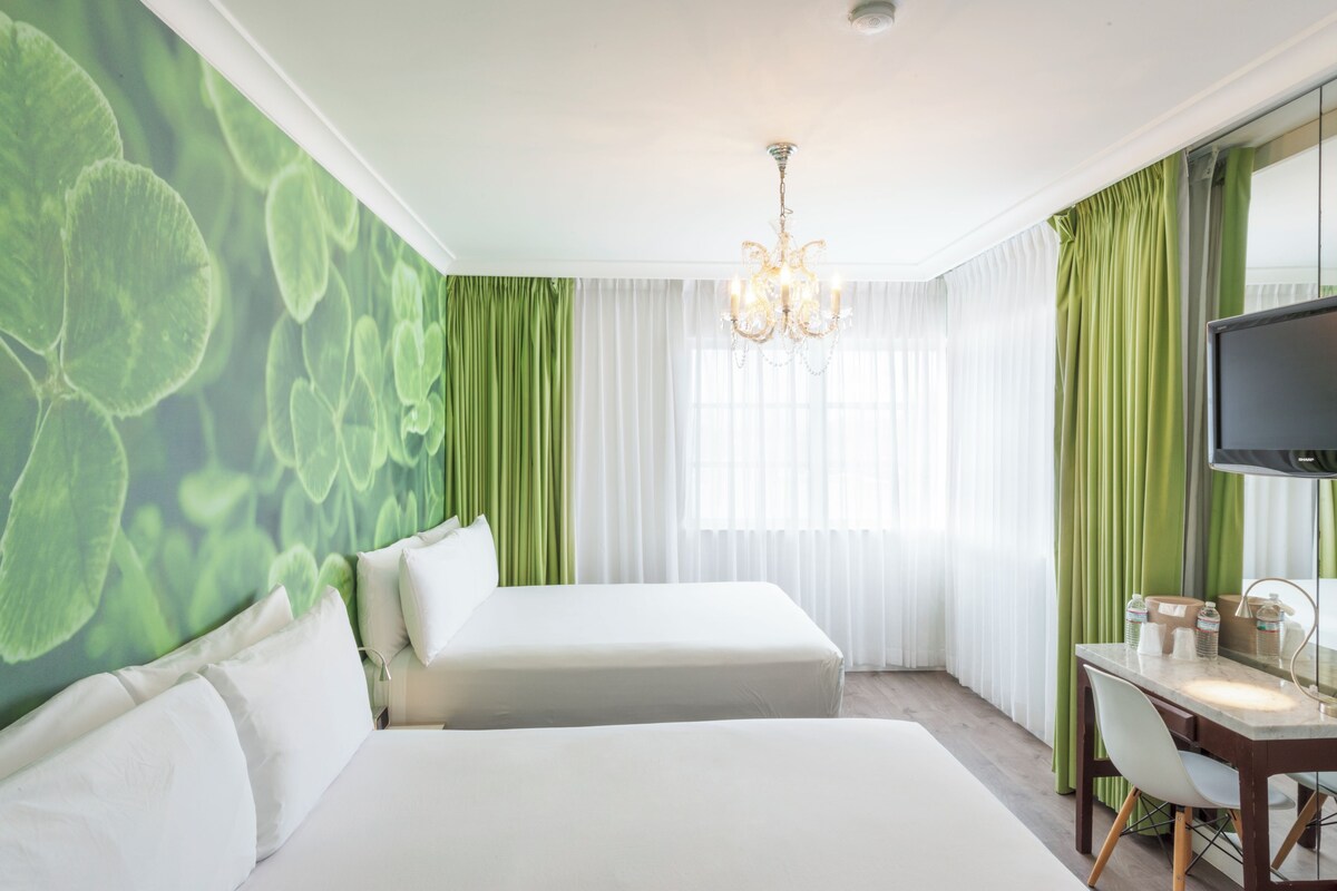 A hotel room with two beds, a desk, a television, and a large window with curtains.