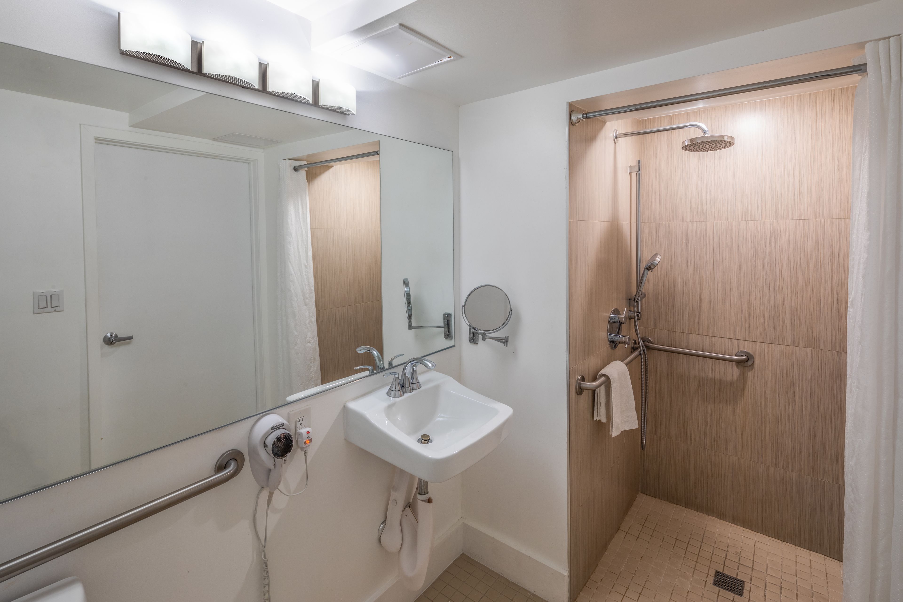 A modern bathroom with a white sink, a mirror, a handheld showerhead, and a glass shower enclosure.