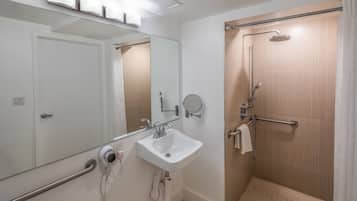 A modern bathroom with a white sink, a mirror, a handheld showerhead, and a glass shower enclosure.