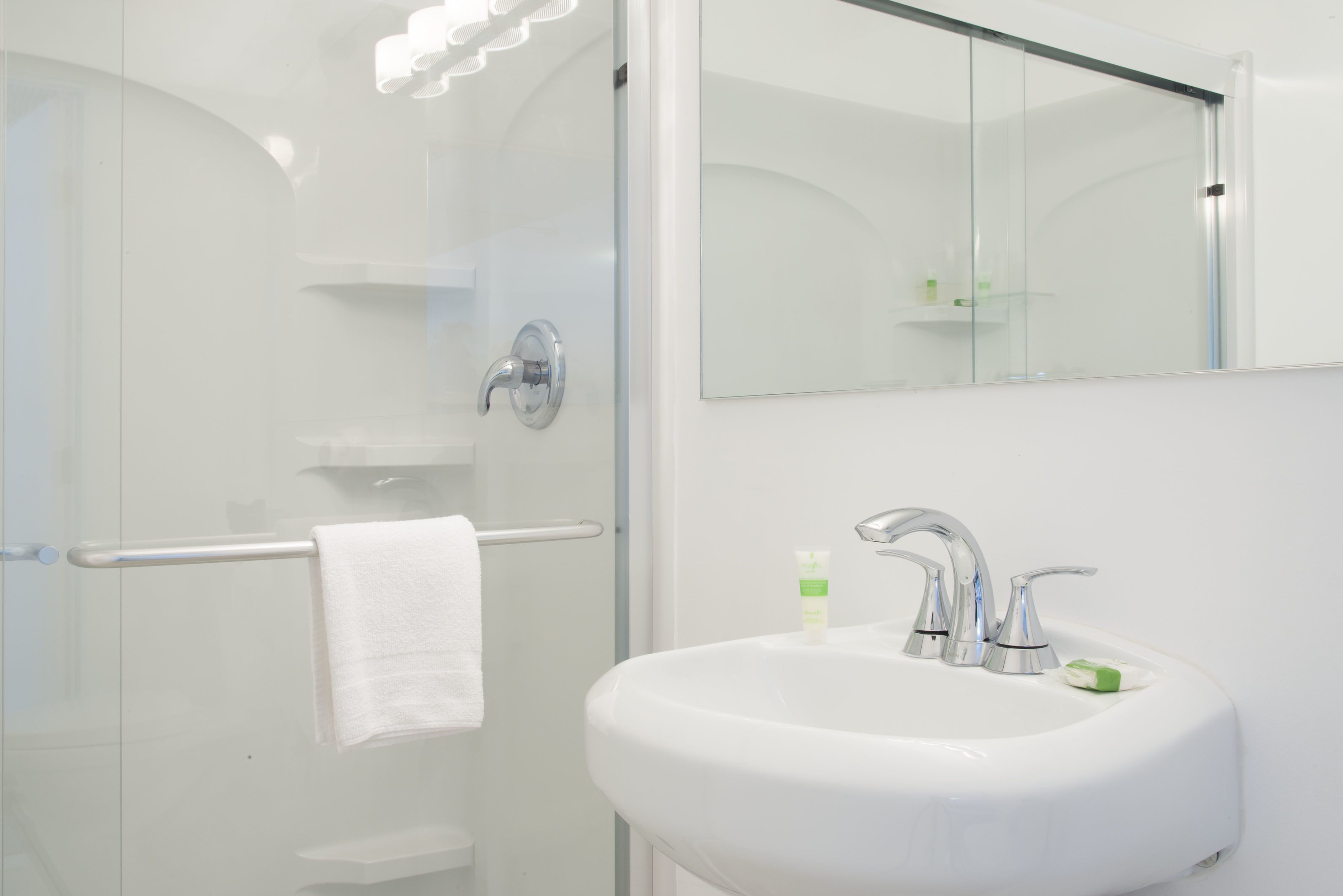 Ein modernes Badezimmer mit einer Duschkabine aus Glas, einem weißen Waschbecken mit Spiegel darüber und einem Handtuchhalter.