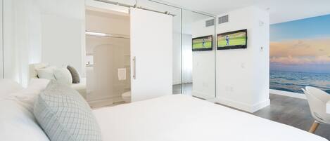 Un dormitorio moderno con una cama grande, un armario de vidrio y un televisor mostrando un partido de golf.