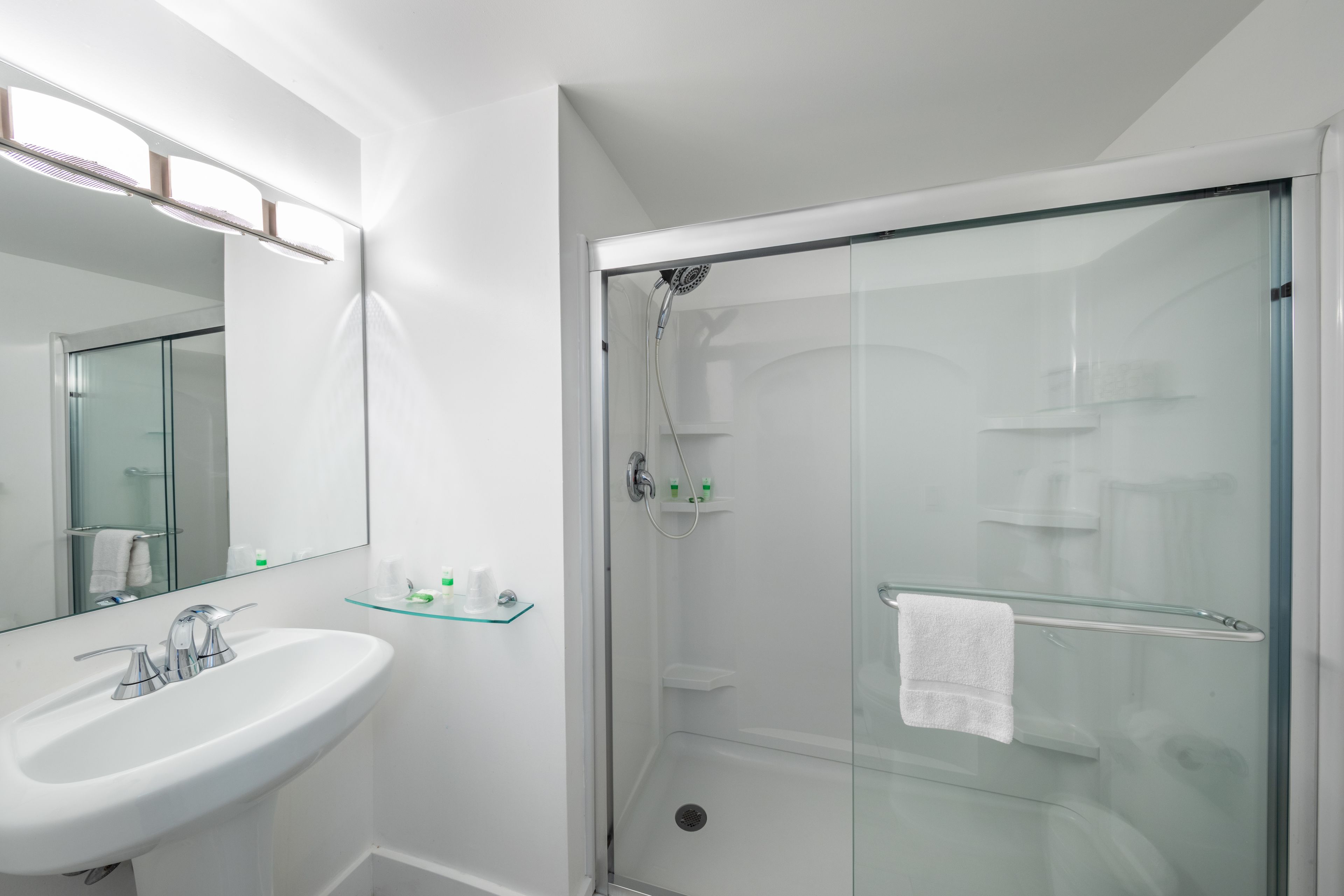 A modern bathroom with a glass-enclosed shower, a white sink, and a glass shelf with toiletries.