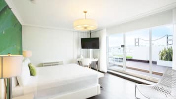 Una habitación de hotel moderna con una cama grande, un escritorio, un televisor y un balcón con vistas a la ciudad.