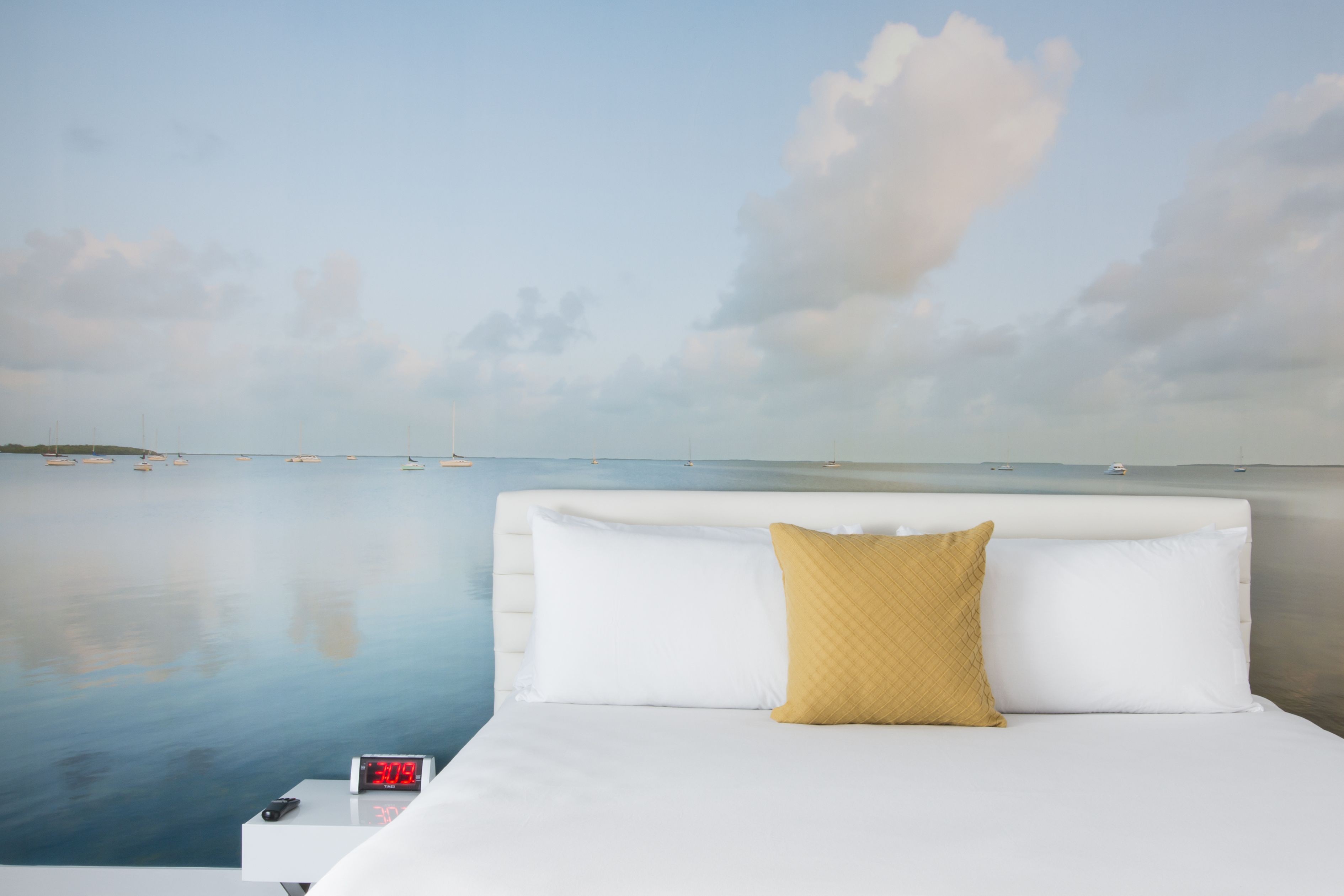 A bedroom with a bed, a nightstand, a digital clock, and a view of the sea.