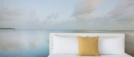 A bedroom with a bed, a nightstand, a digital clock, and a view of the sea.