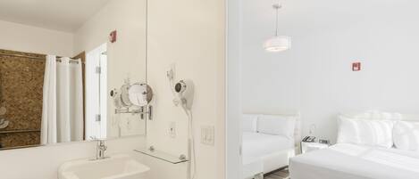 A modern hotel room with a large bed, a bedside table, a mirror, a sink, and a hairdryer.