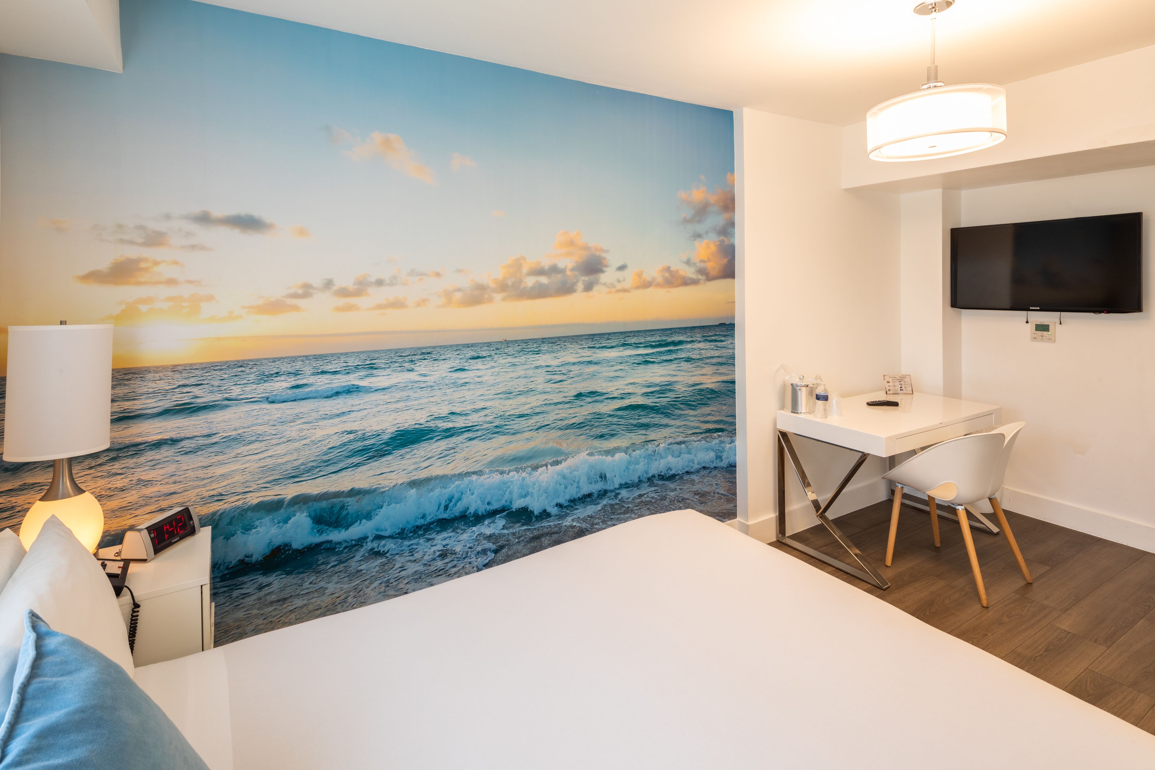 Une chambre avec un grand décor mural représentant l’océan, un lit, un bureau avec une chaise, une télévision et une lampe.