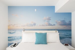 A bedroom with a bed, a nightstand, a digital clock, and a wall mural of the ocean.