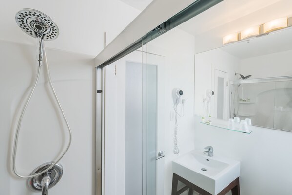 A modern bathroom with a glass shower enclosure, a white sink, and a glass shelf above the mirror.