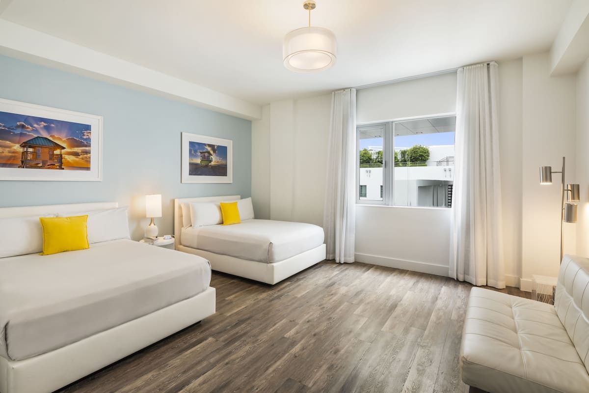 A hotel room with two beds, a large window with curtains, and artwork on the walls.