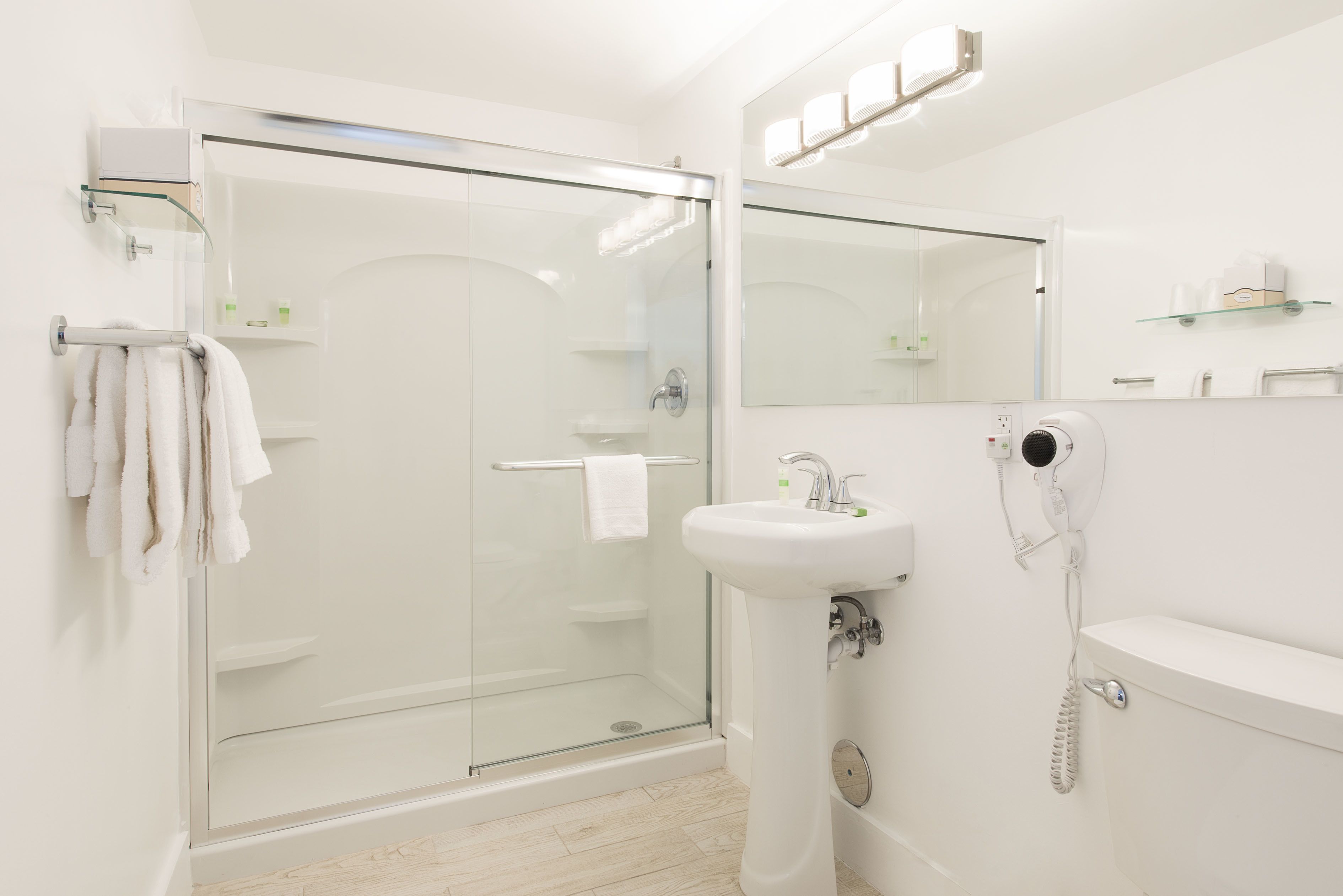 A modern bathroom with a glass-enclosed shower, a white sink, and a hairdryer mounted on the wall.