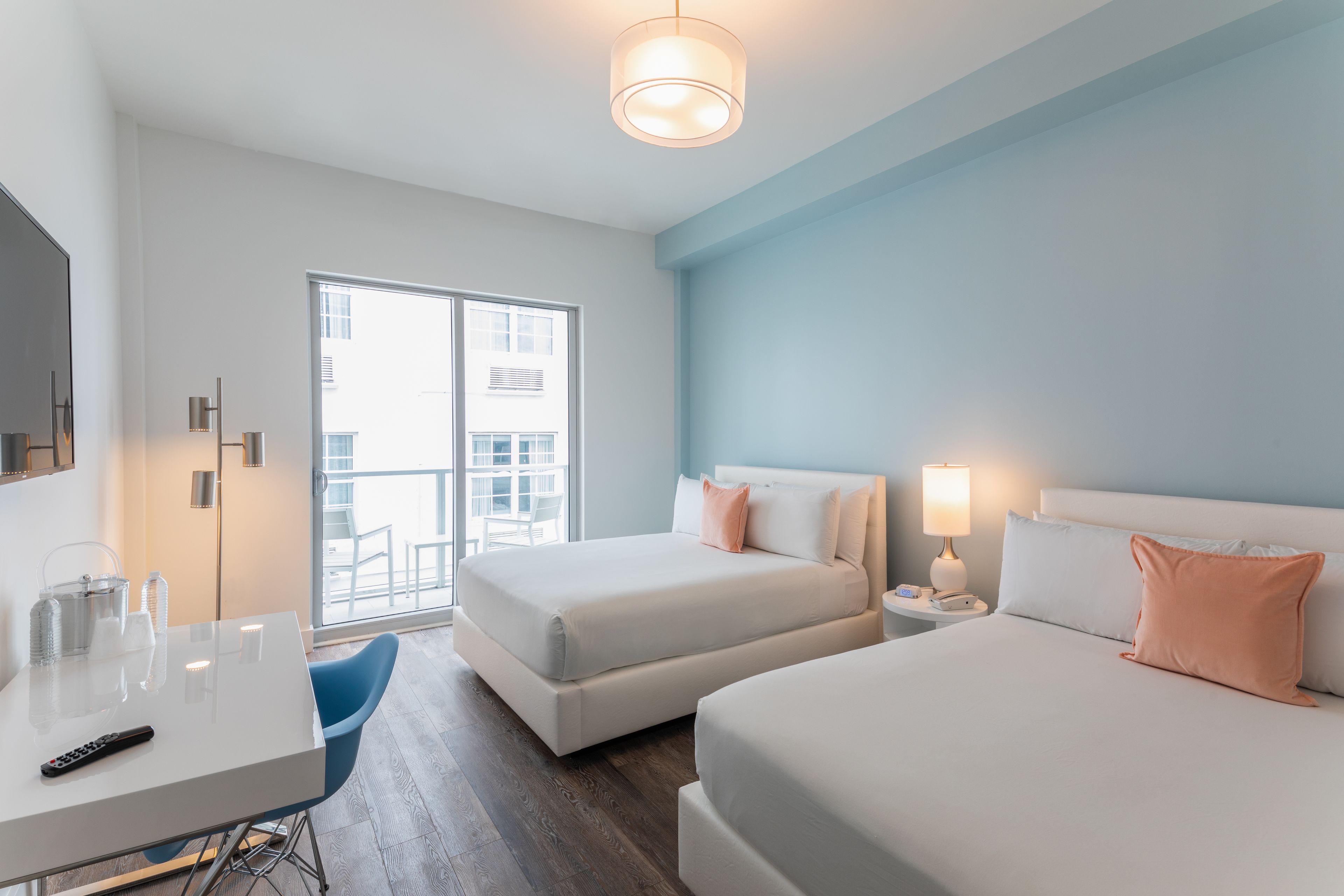 A modern hotel room with two beds, a desk, and a balcony with a view.