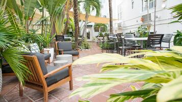 Un patio al aire libre con mobiliario de madera, piso de baldosas y diversas plantas.