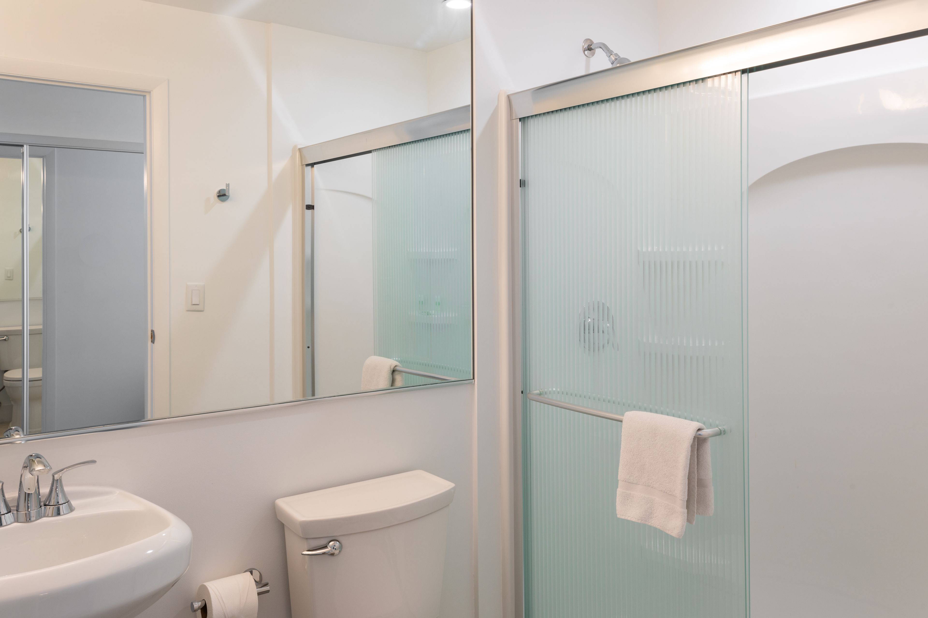 Een moderne badkamer met een glazen douchecabine, een witte wastafel en een toilet.