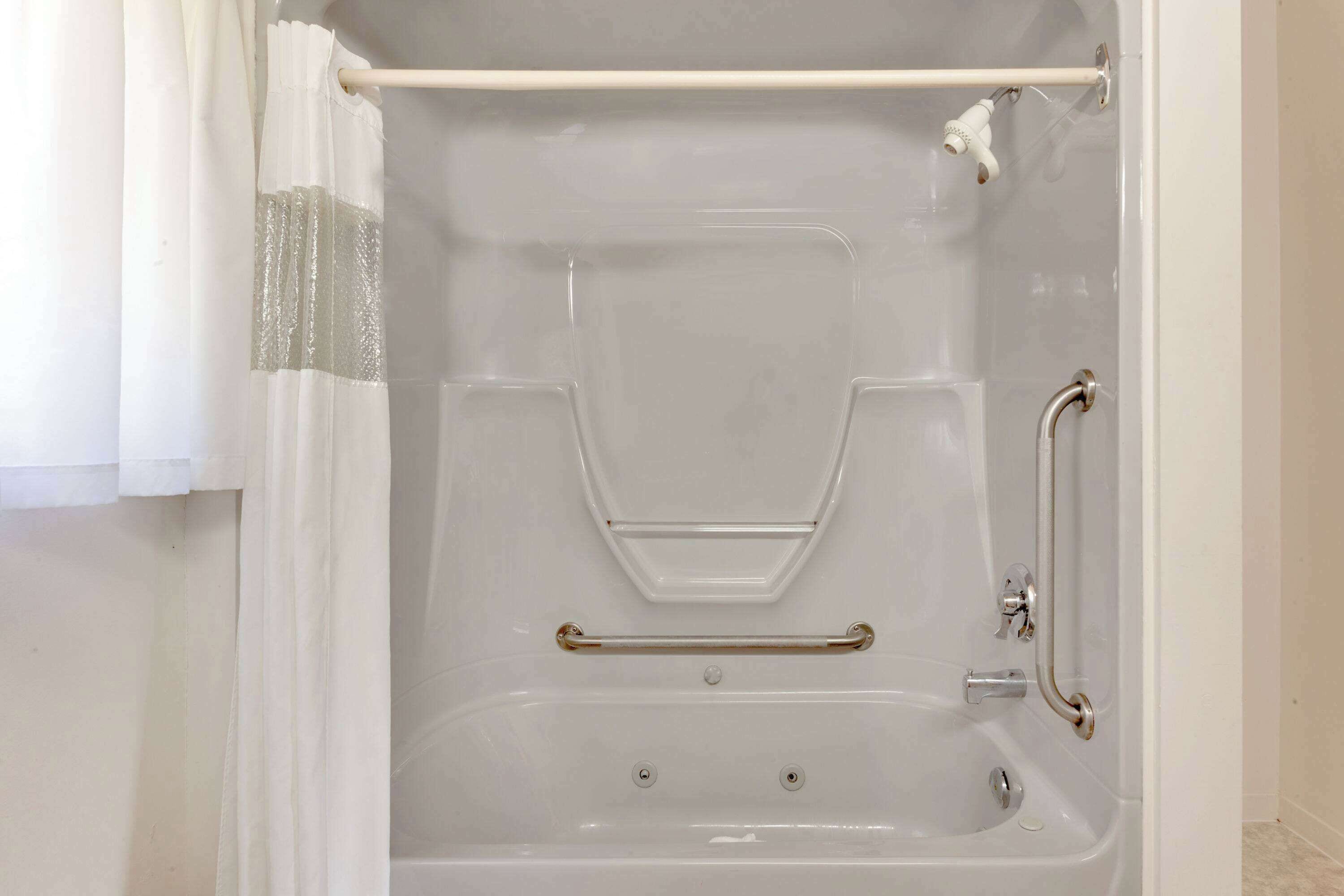 A white bathtub with a shower curtain, grab bars, and a handheld showerhead.