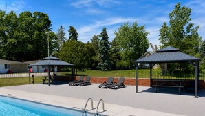 A swimming pool with lounge chairs and gazebos, surrounded by a brick wall and a fence. - Ramada by Wyndham 1000 Islands/Gananoque (Gananoque)